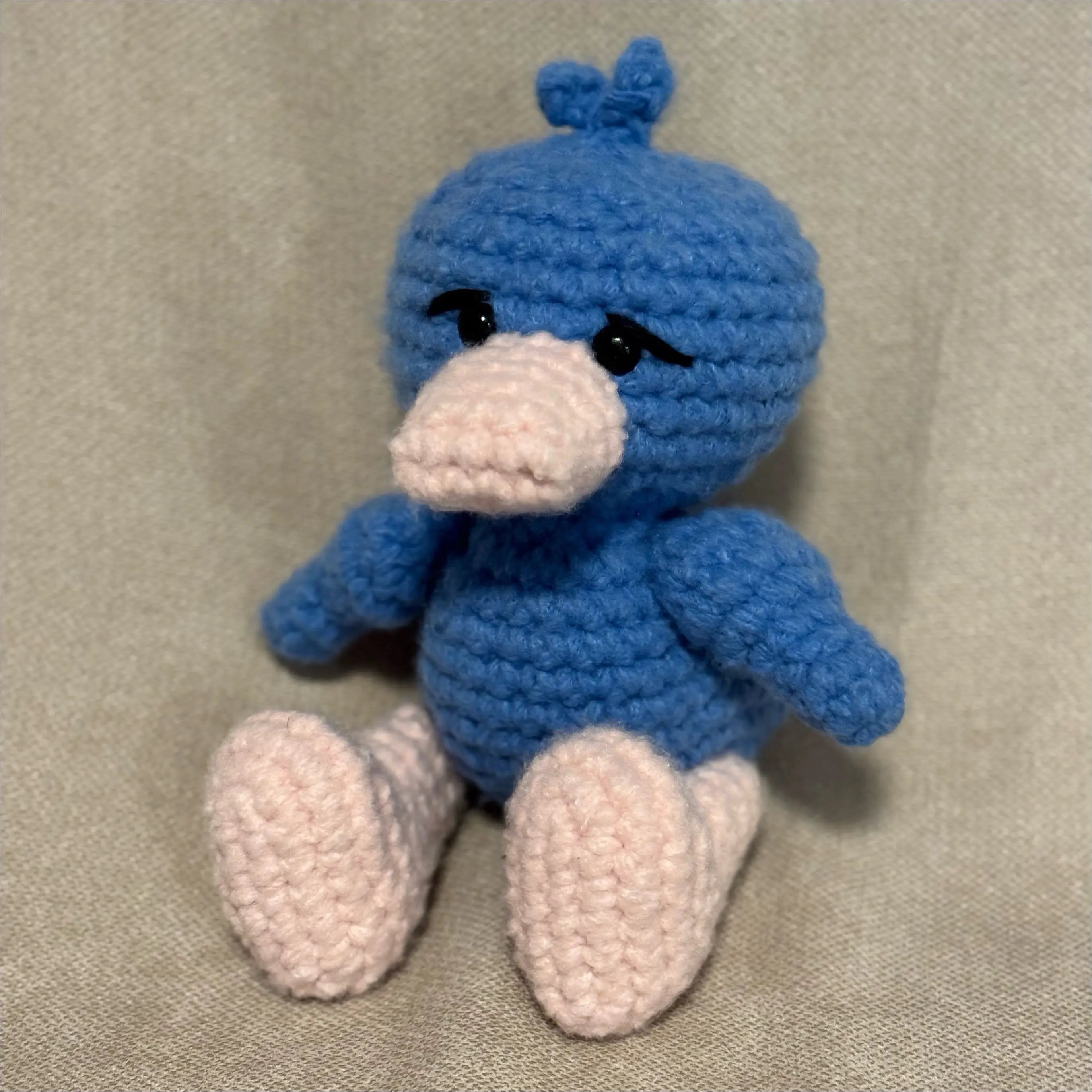 Blue crochet duck toy on a beige fabric background