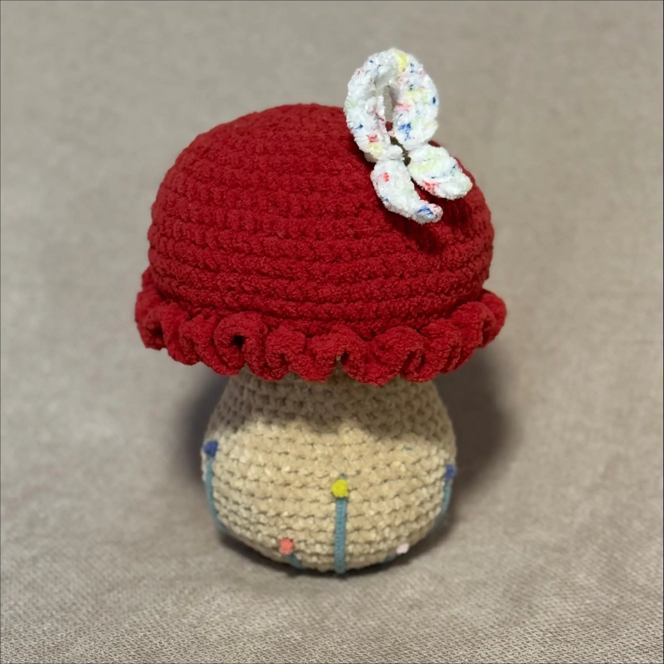 Crocheted mushroom with a red cap and decorative band on a beige background