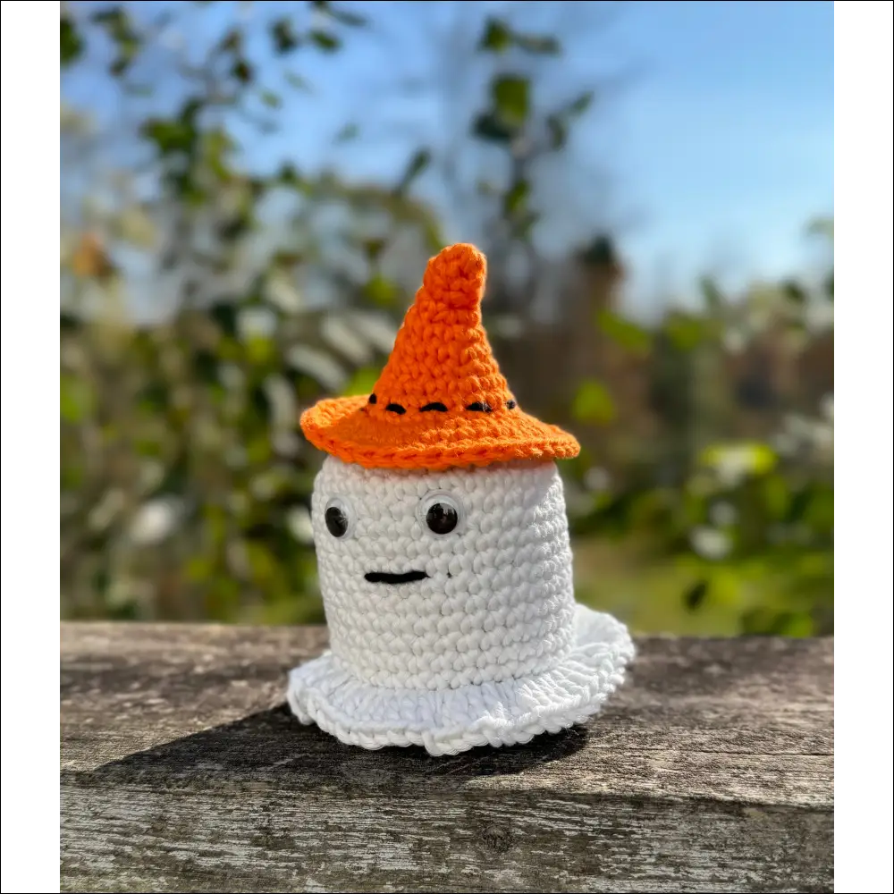 Crocheted white glowing ghost figure wearing an orange pointed hat for Halloween fun