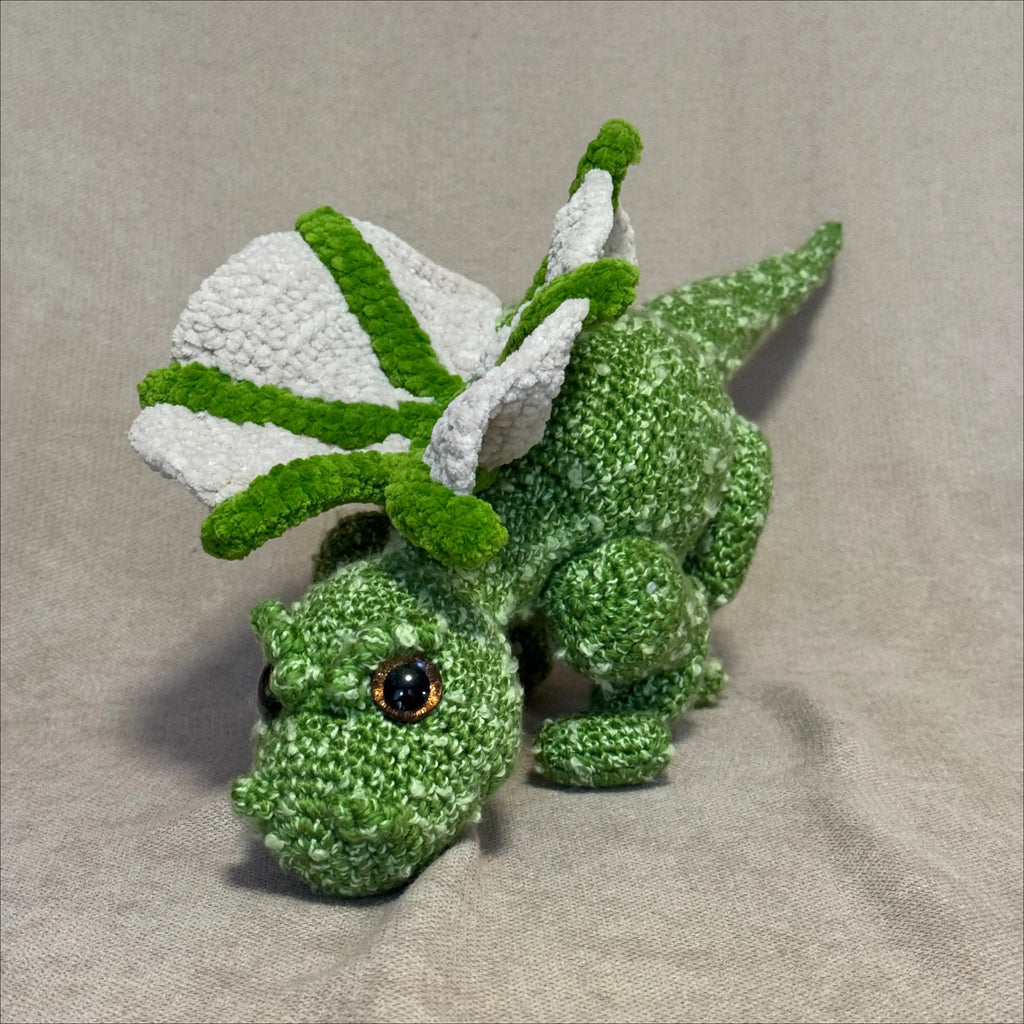 Green crocheted dragon toy on a beige fabric background