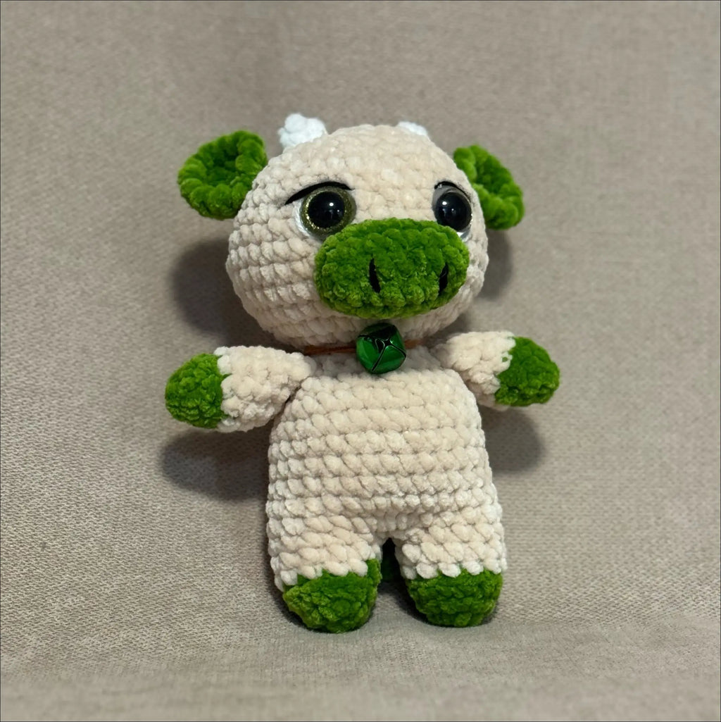 Crocheted cow toy with green accents on a beige background