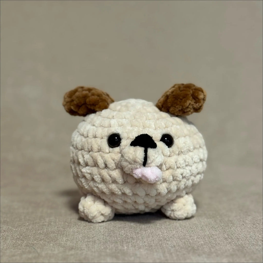 Crocheted dog toy with brown ears and a pink nose on a beige background