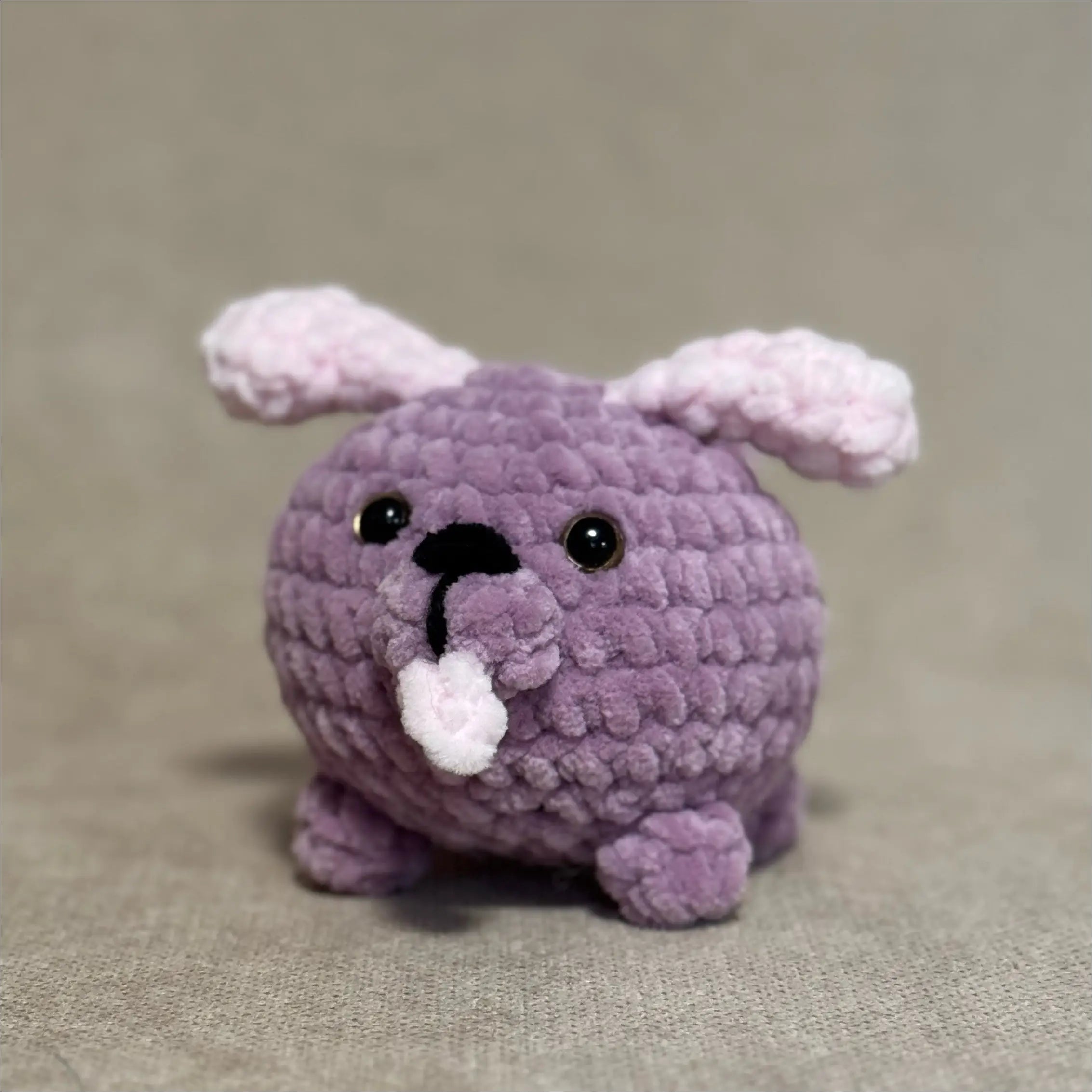 Purple crochet dog toy with pink ears on a beige background