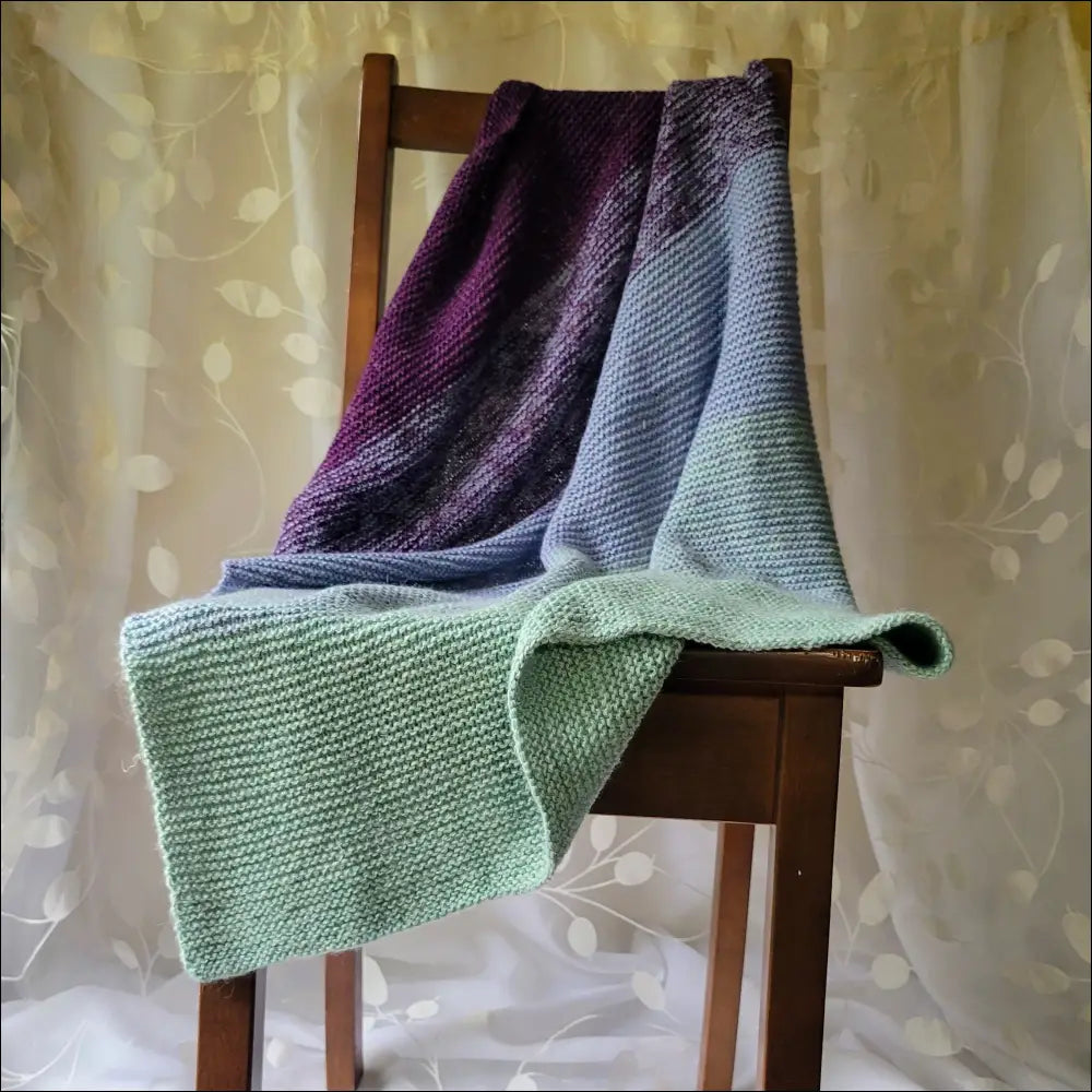 Cozy Luxe Gradient Baby Blanket in purple, blue, and green draped over a wooden chair