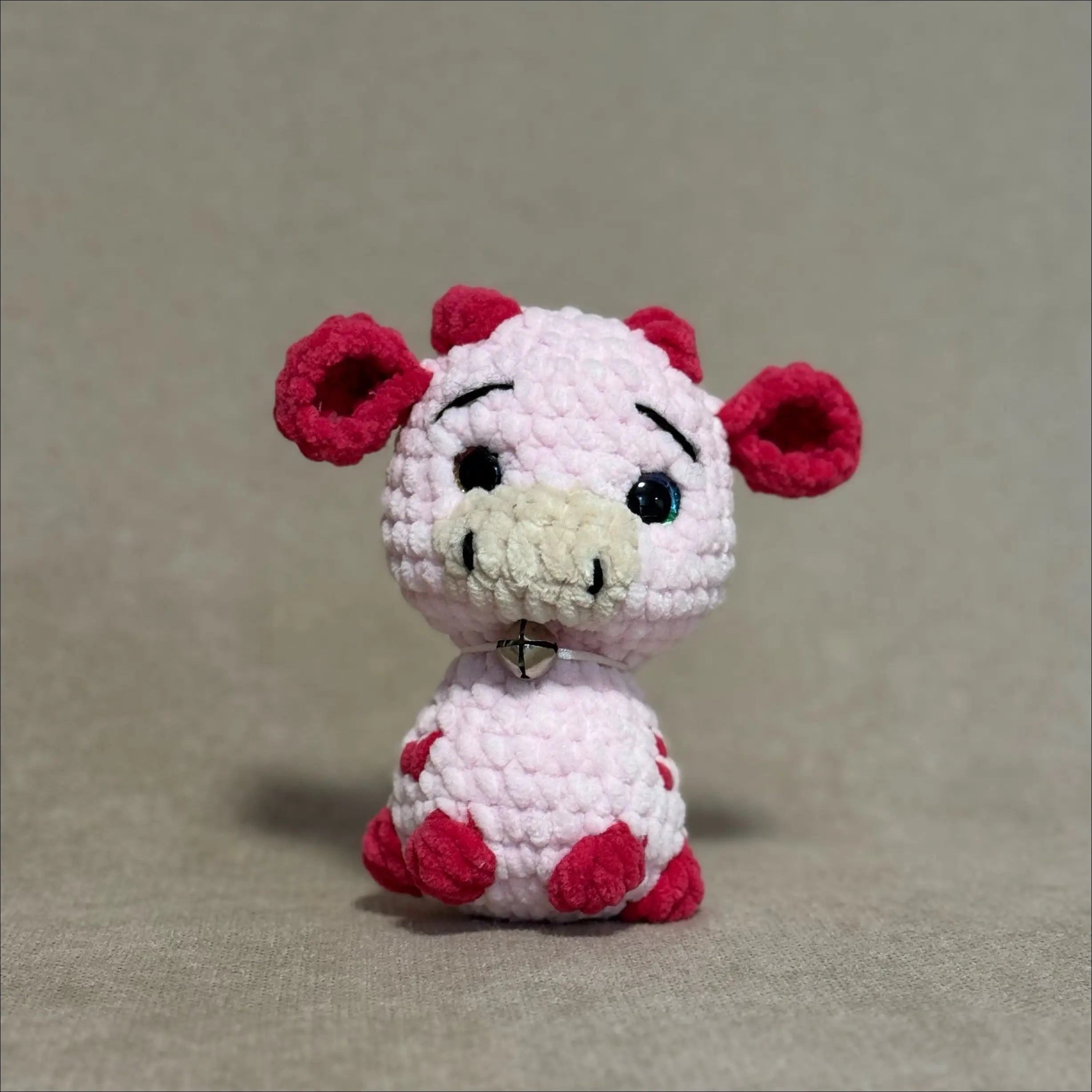 Small crochet cow toy with pink body  on a beige background