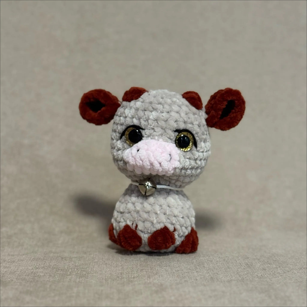 Small crochet cow toy with brown ears on a beige background