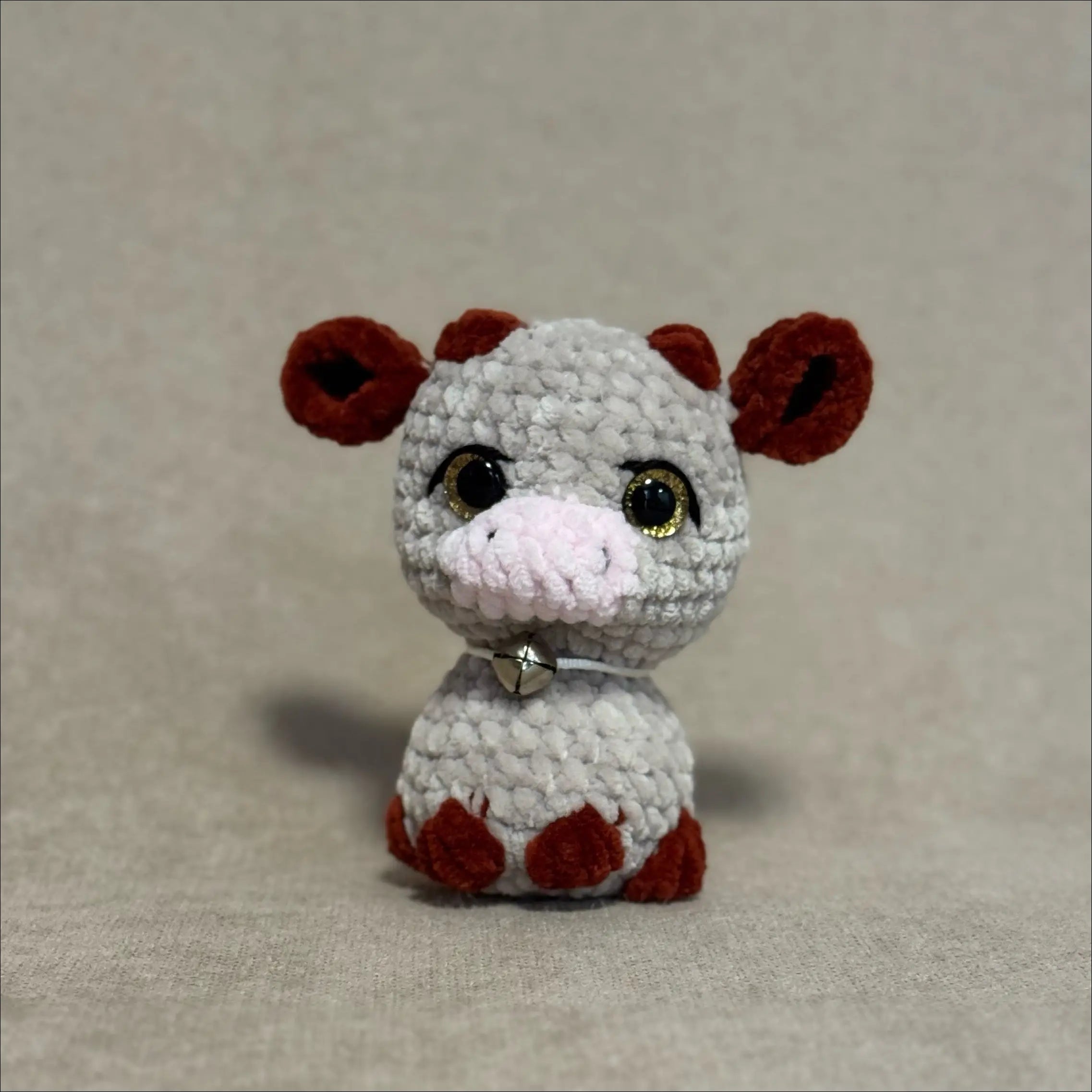 Small crochet cow toy with brown ears on a beige background
