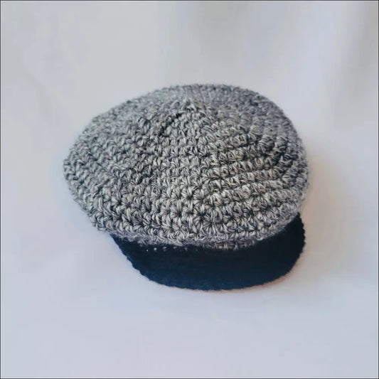 Gray crocheted newsboy cap for kids with a black brim and handmade charm