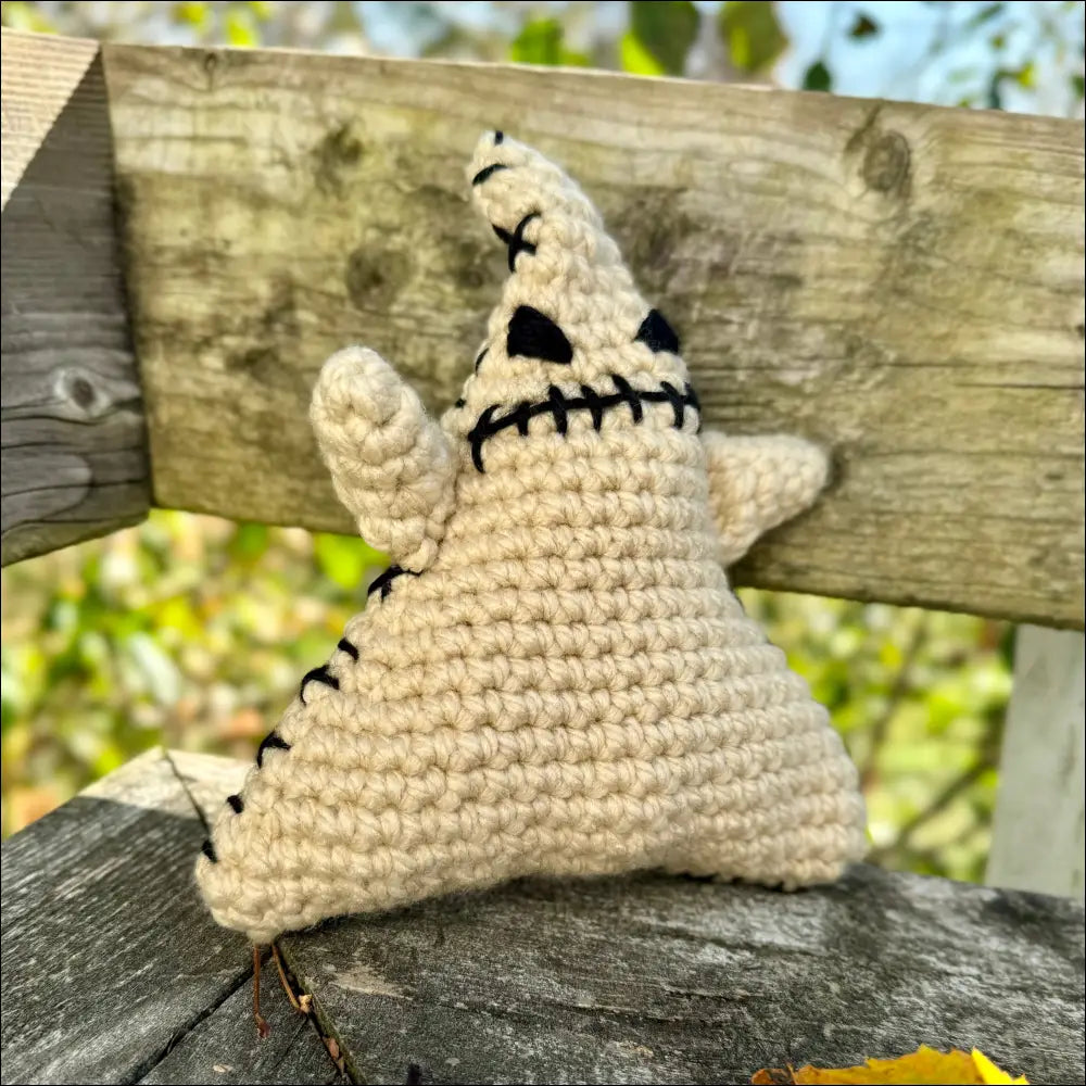 Crocheted Spooky Oogie Boogie Plush ghost figure with a stitched face on wood