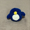 Small blue crocheted penguin toy on a beige fabric background