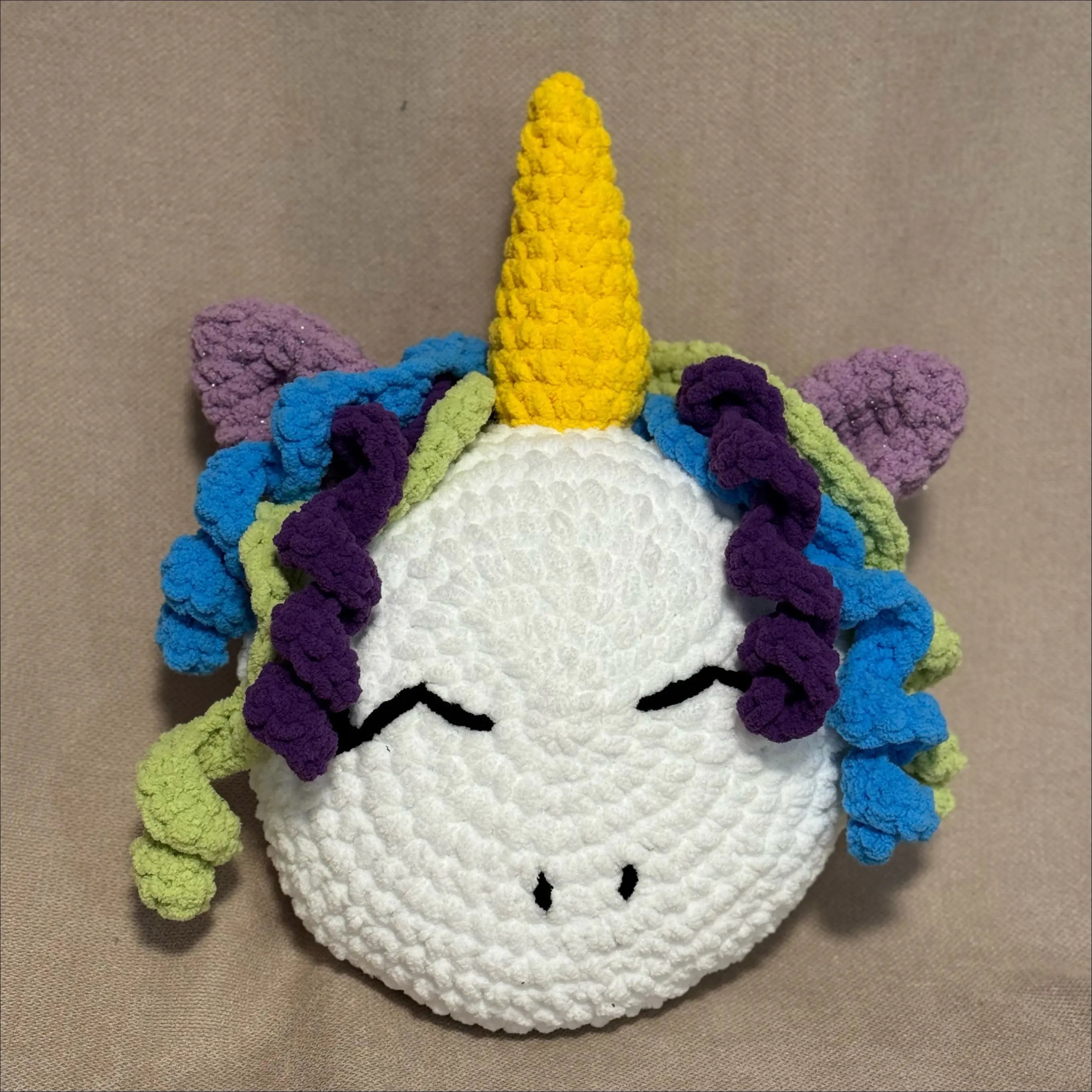 Crocheted unicorn pillow with a yellow horn and colorful mane on a beige background