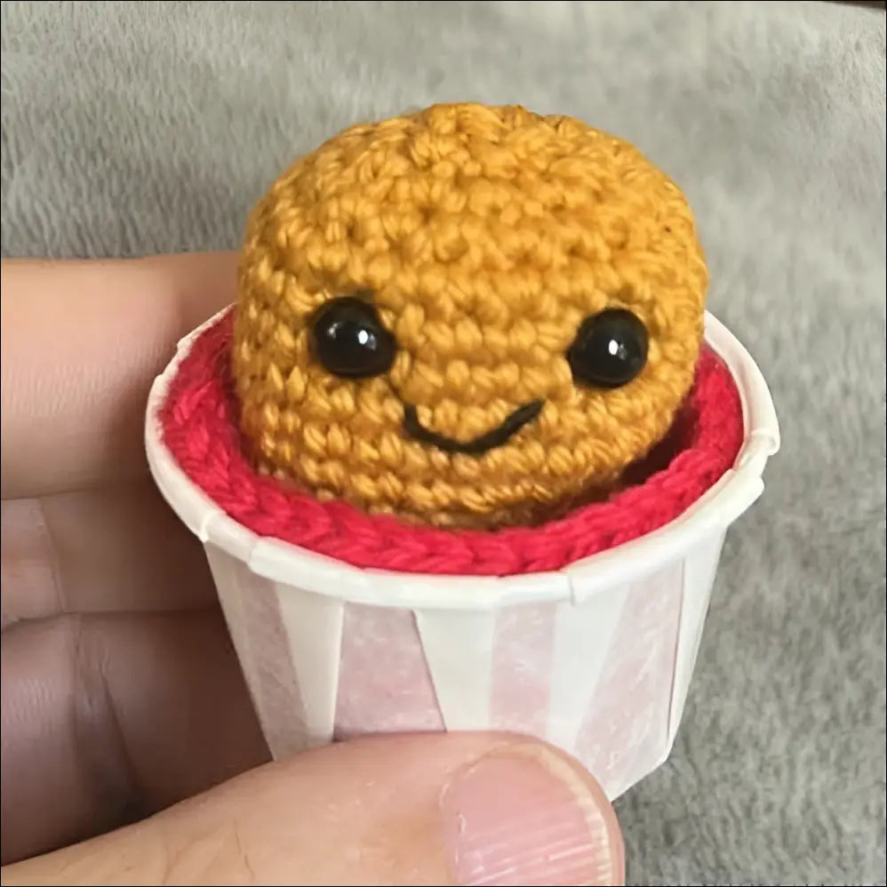 Small crocheted nugget in a red cup held by a hand in a casual setting.