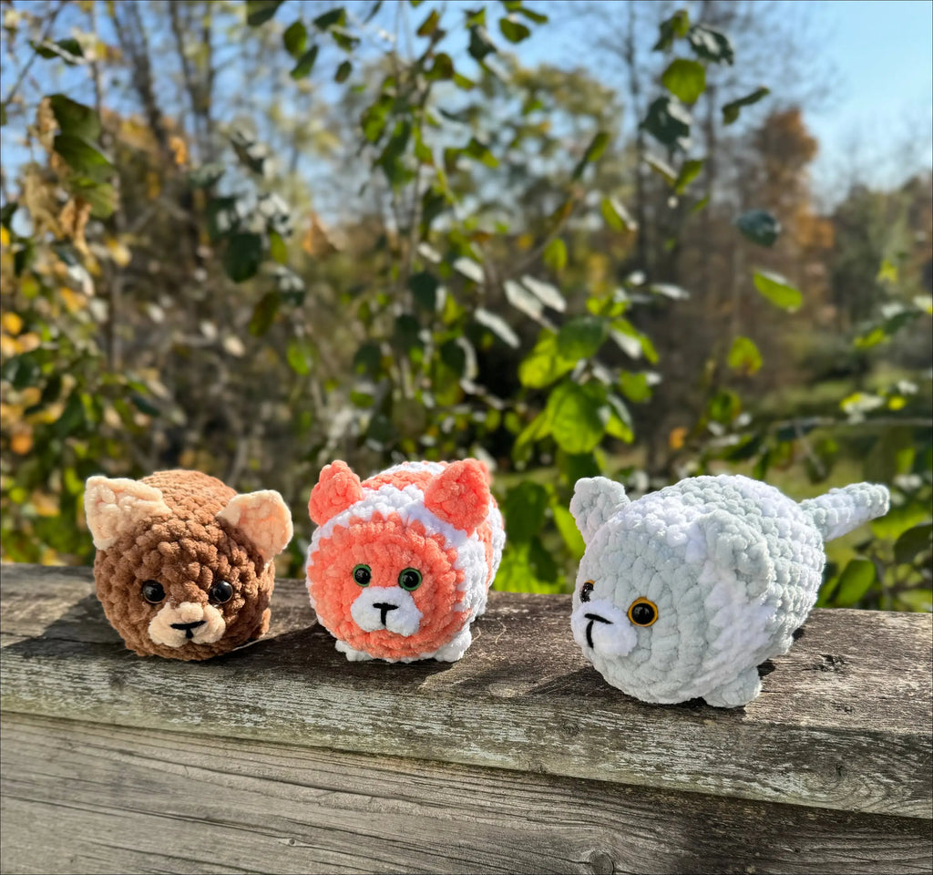 Three plump kitty plush toys like cuddly round balls on a wooden surface