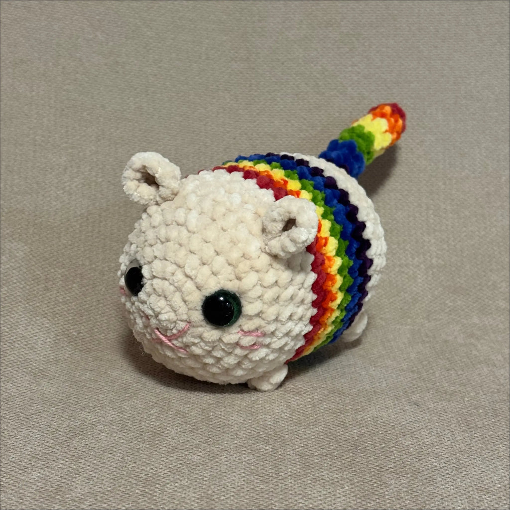 Crocheted unicorn plush toy with a rainbow mane on a beige background