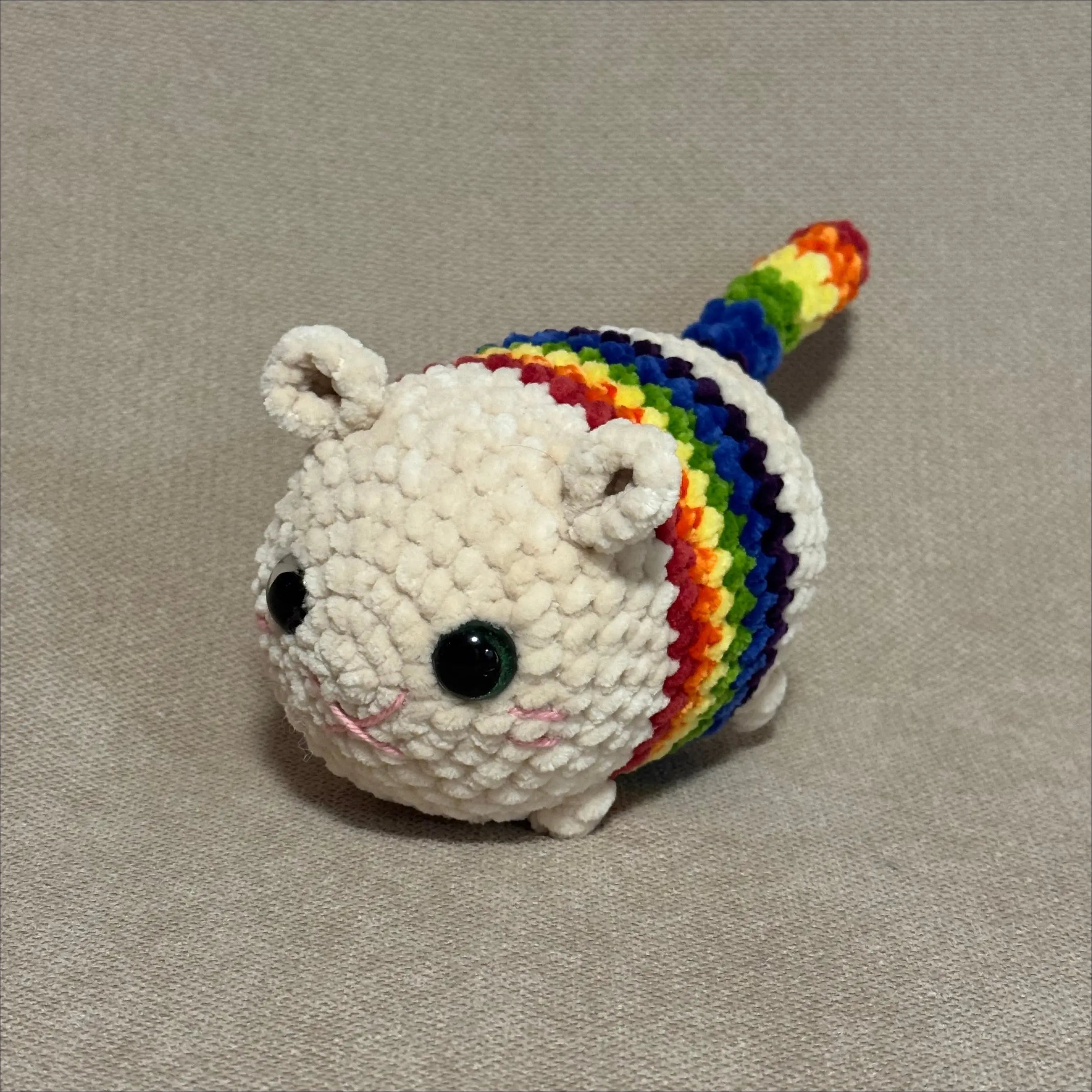 Crocheted unicorn plush toy with a rainbow mane on a beige background