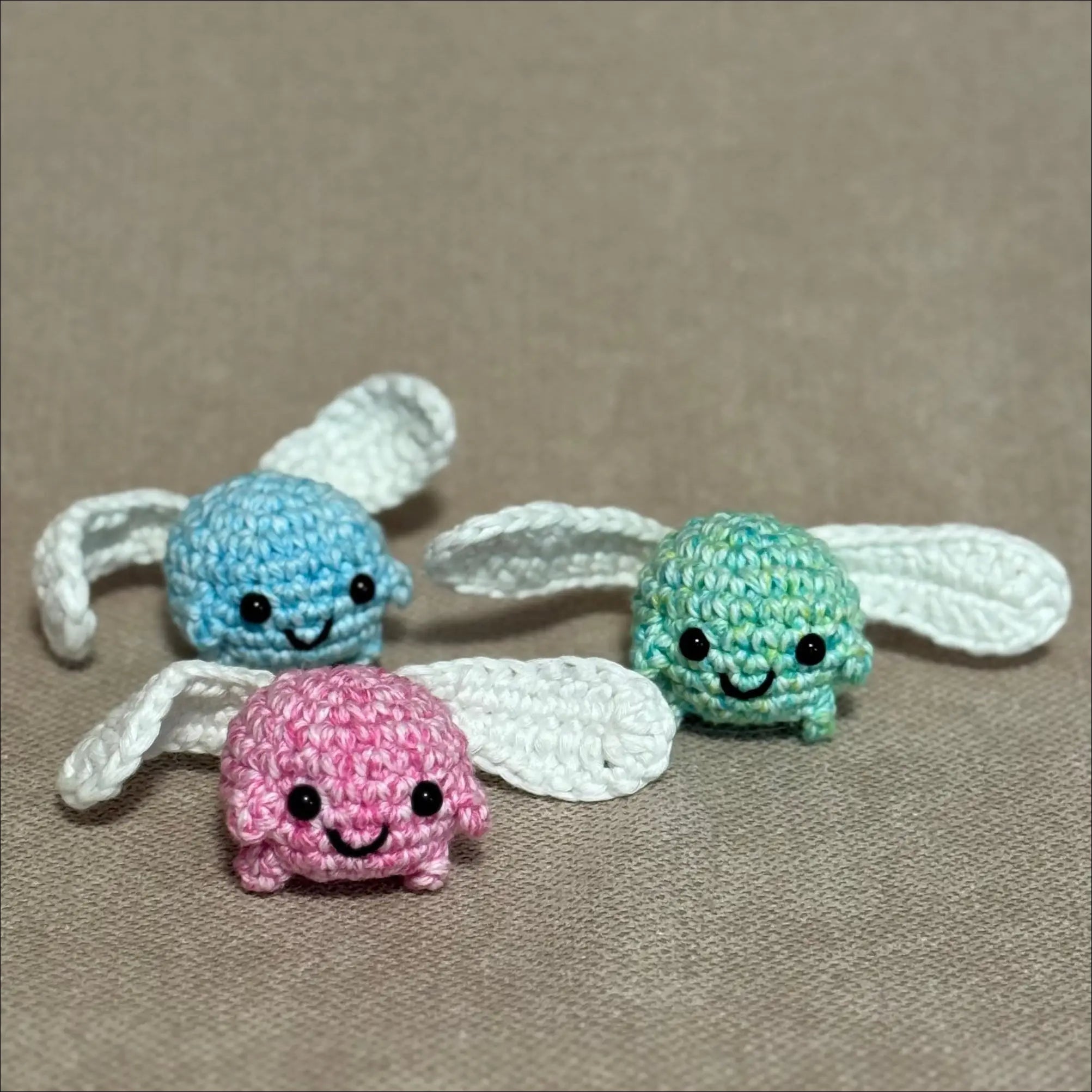 Three colorful crochet sprites with glow in the dark wings on a beige background