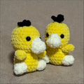 Two yellow crochet duck toys with black heads on a gray background