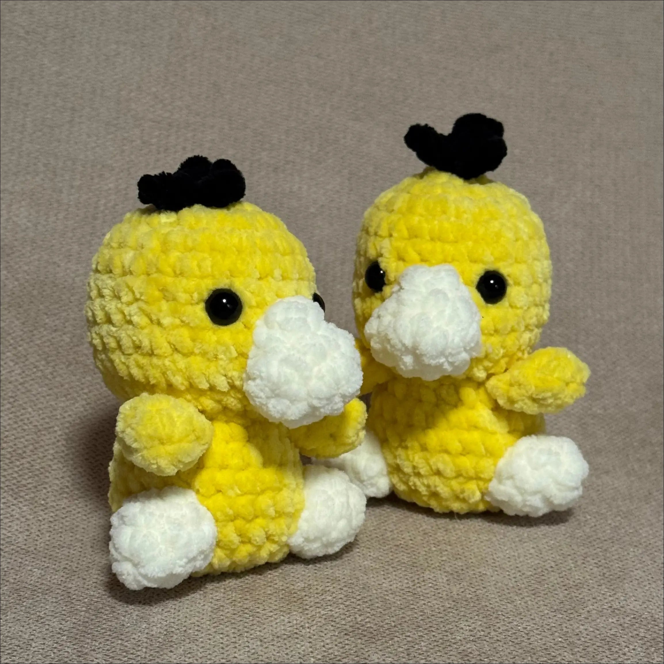 Two yellow crochet duck toys with black heads on a gray background