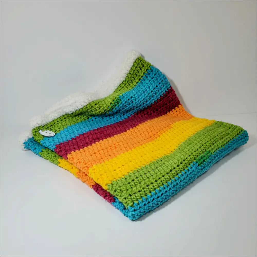 Colorful striped crocheted rainbow blanket folded, perfect for brightening your babe’s room