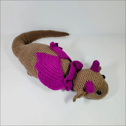 Crocheted brown and magenta resting dragon toy with purple wings and long tail