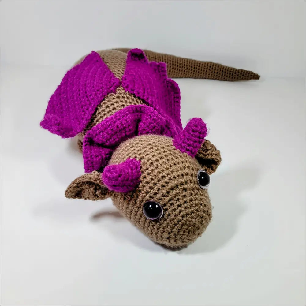 Cute crocheted stuffed resting dragon with tan body and bright purple wings