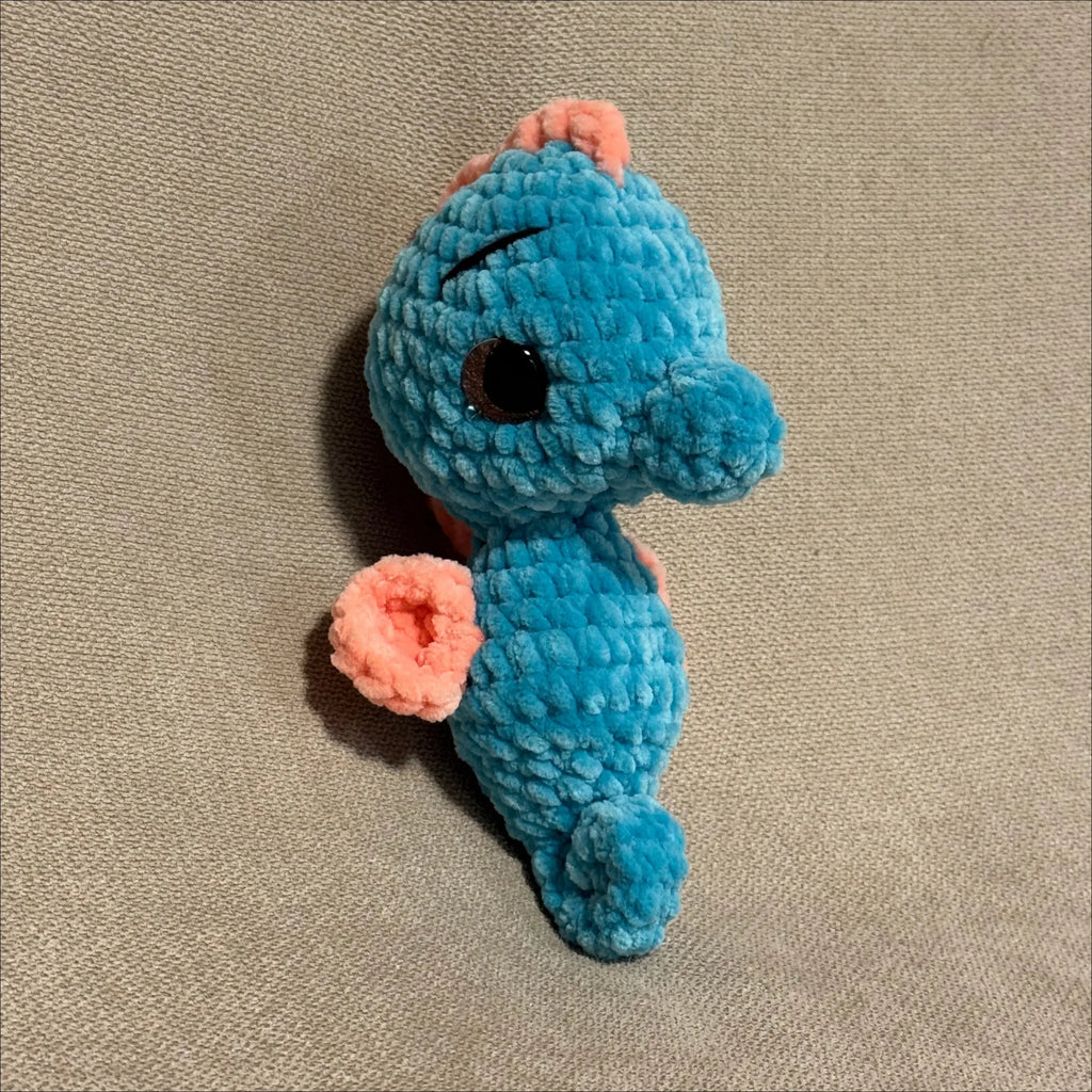 Blue and pink crochet seahorse on a beige fabric background