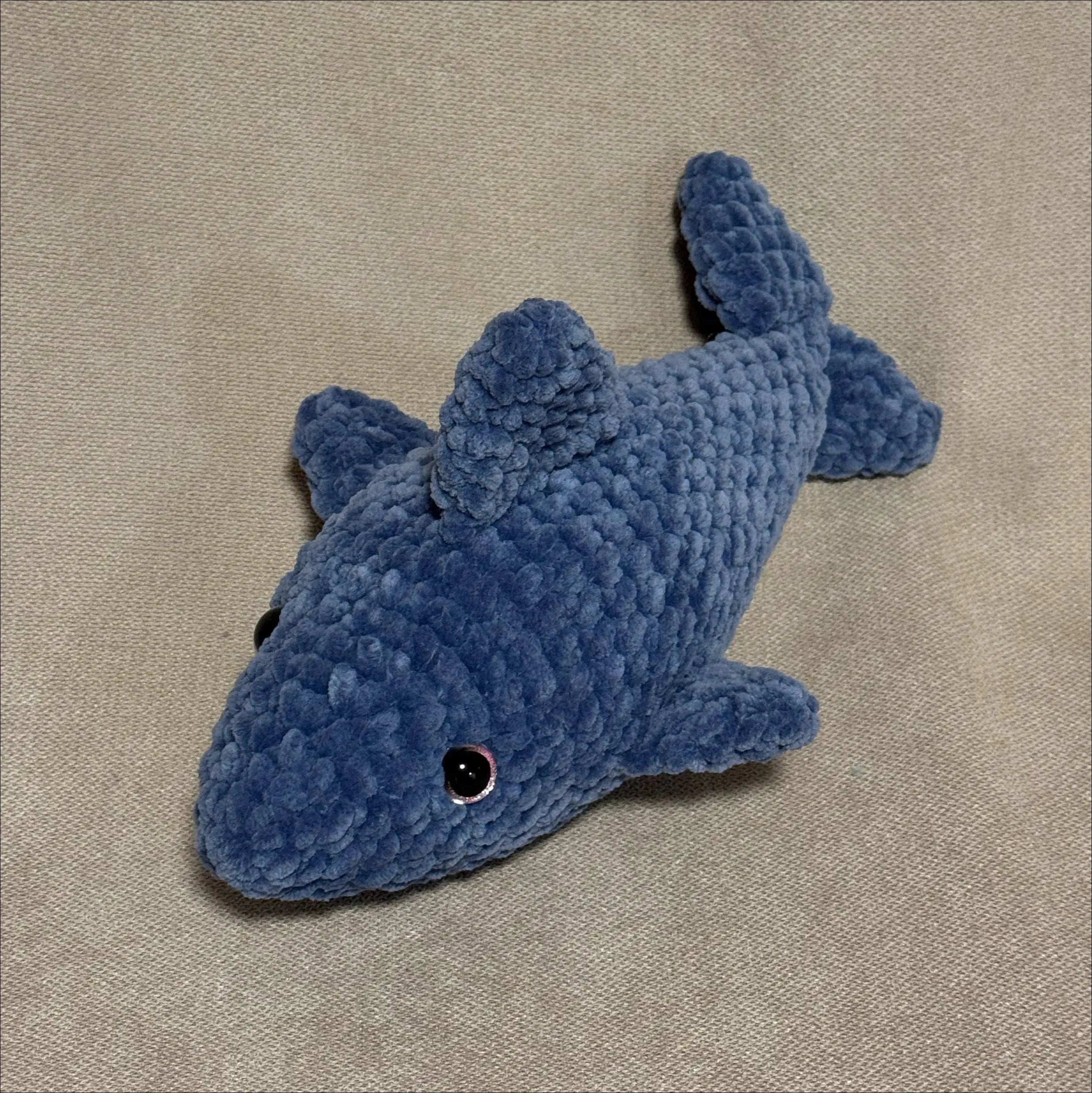 Blue crocheted shark toy on a beige fabric background