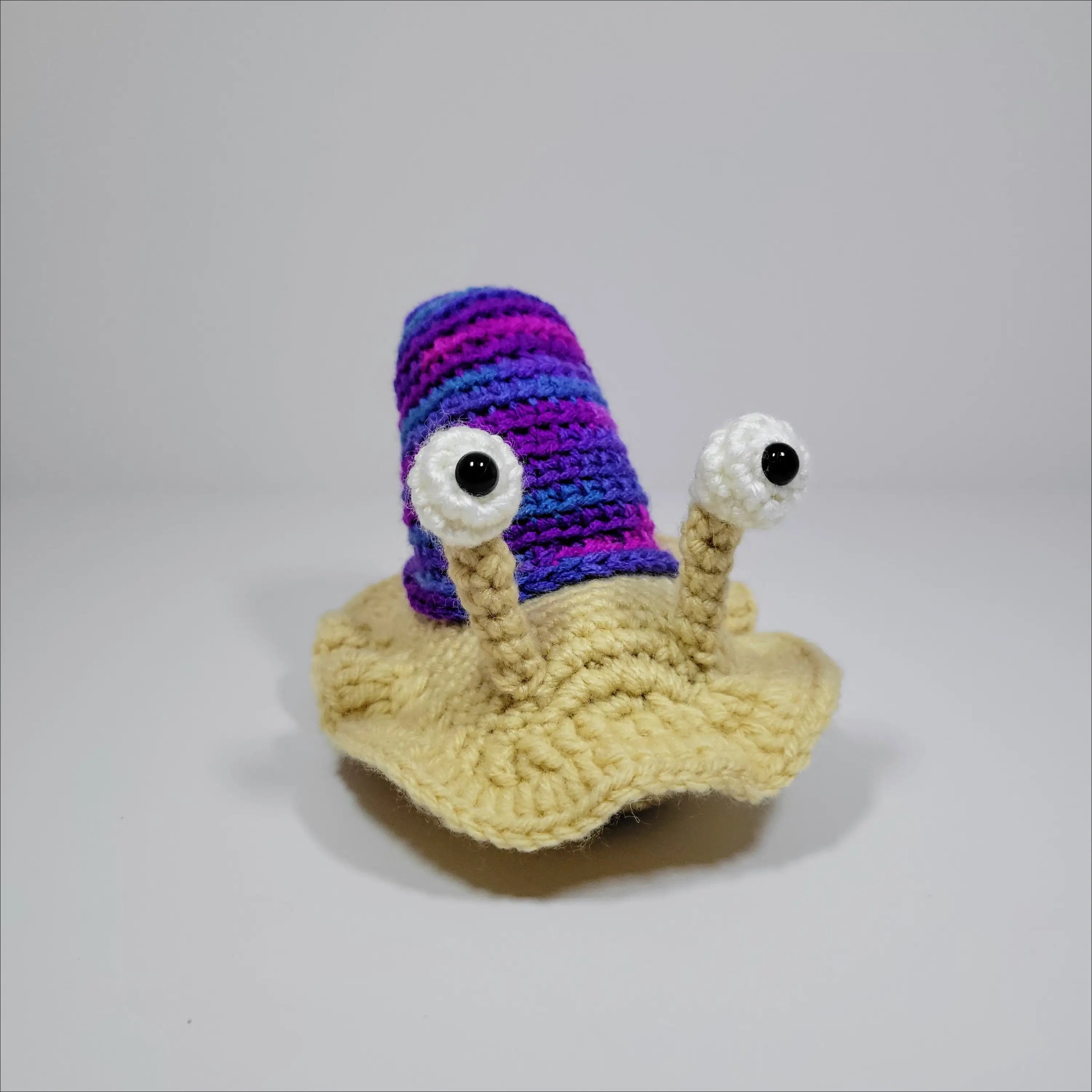 Cute hand-crocheted snail in green yellow and grey pink with a tiny bird on its back