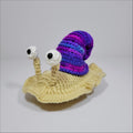 Cute hand-crocheted snail with a purple and blue shell in green yellow and grey pink
