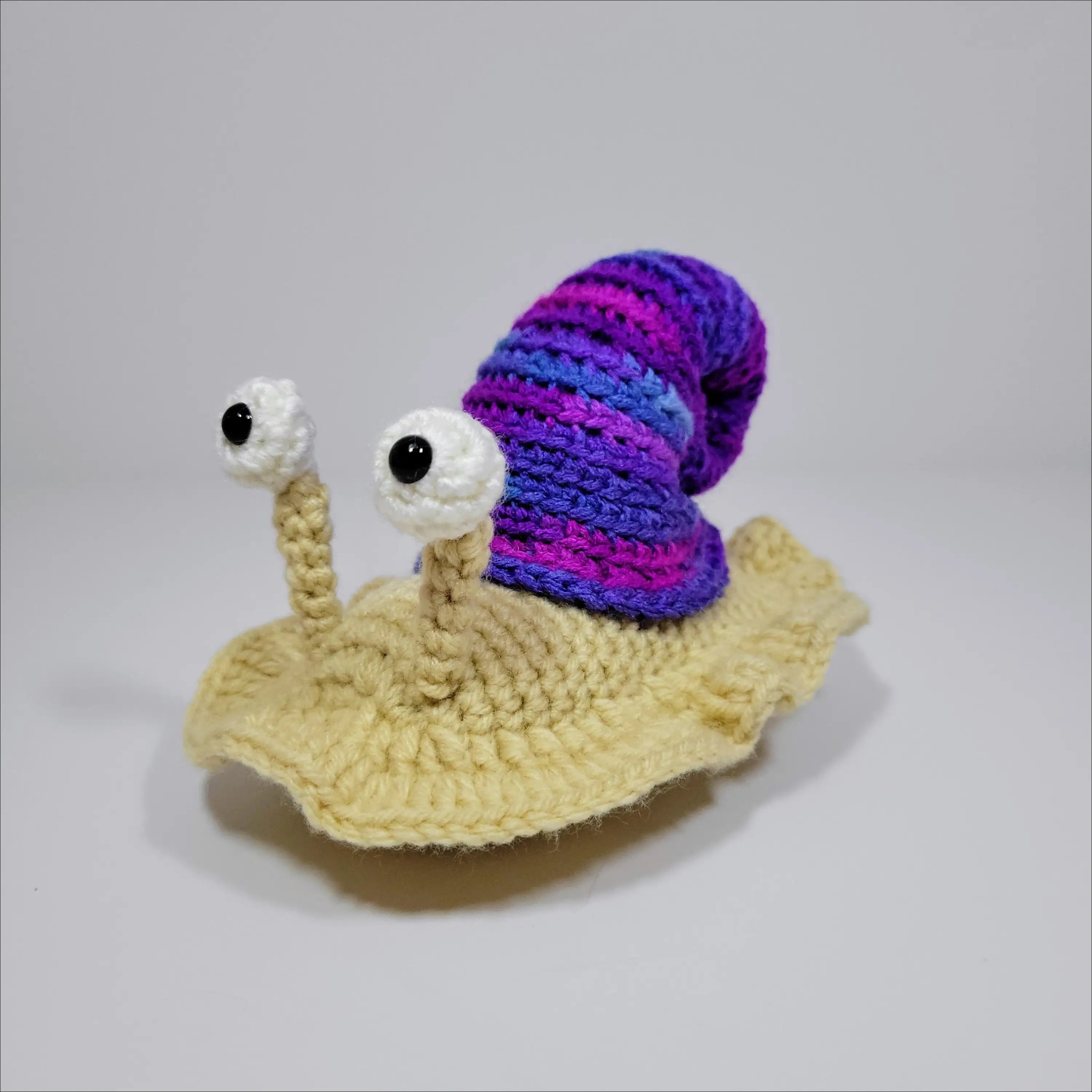 Cute hand-crocheted snail with a purple and blue shell in green yellow and grey pink