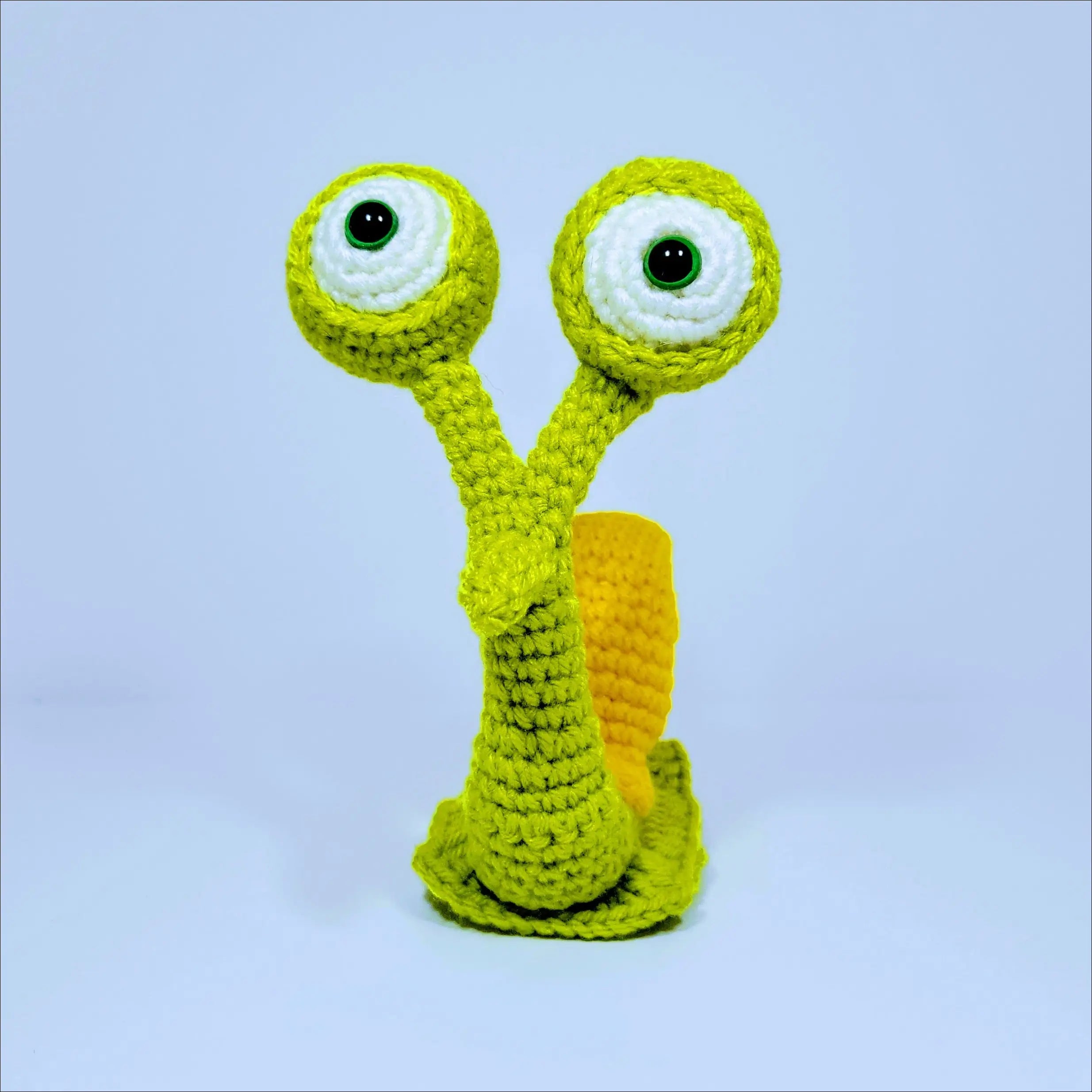 Cute Hand-crocheted Snail toy with a green yellow face against grey pink background