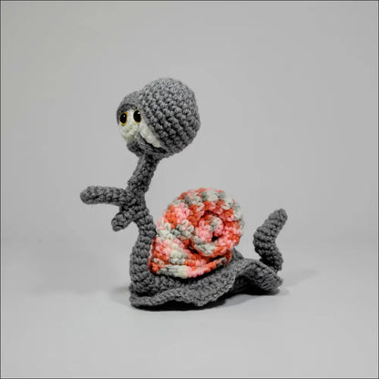 Cute Hand-crocheted Snail toy in green yellow and grey pink on a table