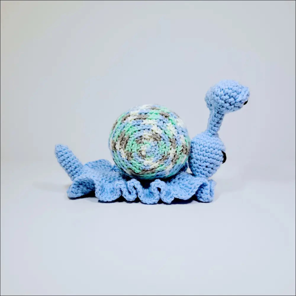 Cute hand-crocheted turtle in blue with a white shell among green yellow and grey pink snails