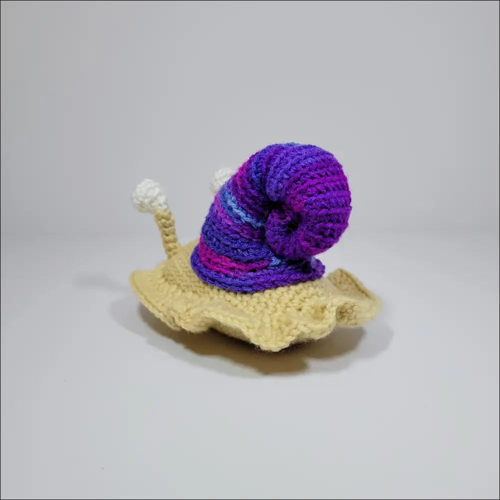 Cute hand-crocheted snail in green yellow and grey pink on a white surface