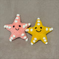 Two starfish toys, one yellow and one pink, on a gray background.
