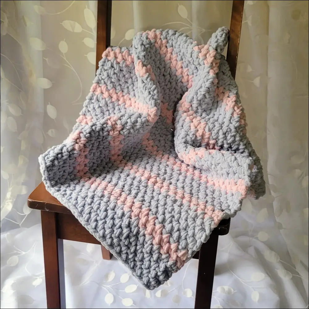 Chunky Sweet Stripes Baby Blanket in gray and pink draped over wooden chair