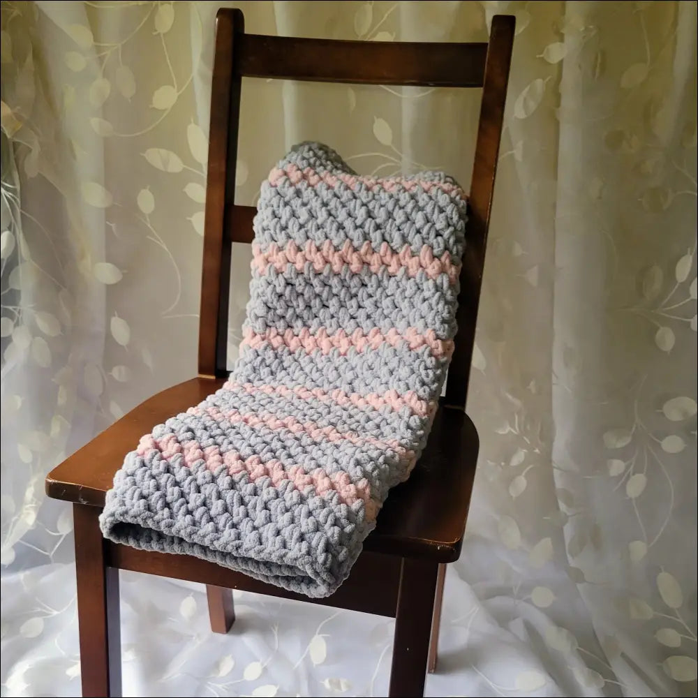 Cozy Sweet Stripes Baby Blanket draped on a wooden chair with gray and pink stripes