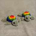 Two plush toys shaped like turtles with rainbow shells on a beige fabric background