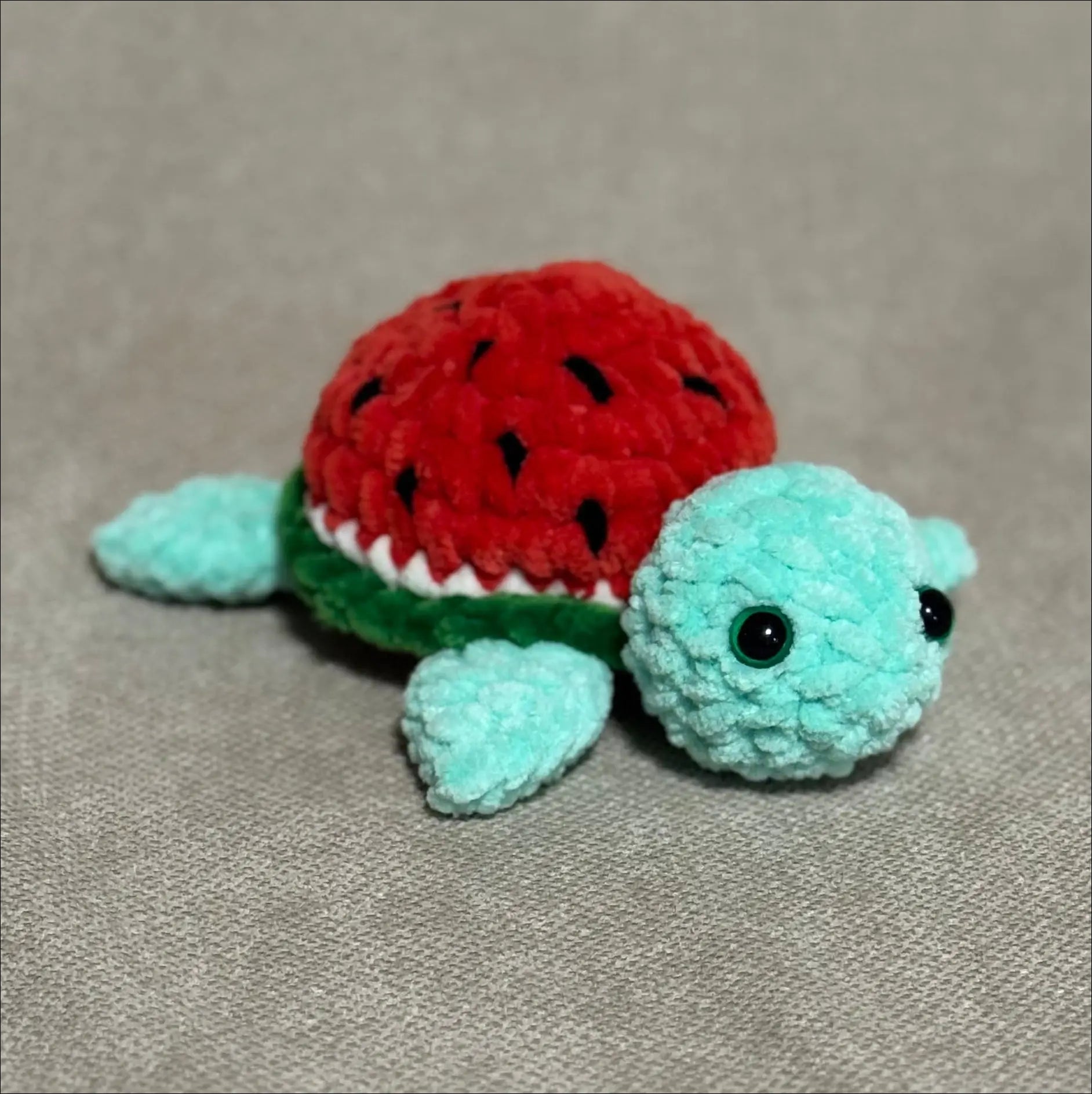 Crocheted turtle toy with red shell on a beige surface