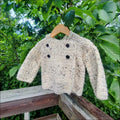 Fluffy beige cozy tweed sweater with wooden buttons hanging on a wooden hanger