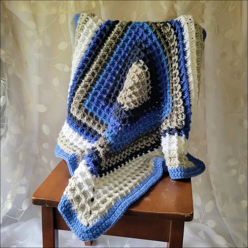 Crocheted waffle baby blanket in blue, white, and gray on a wooden chair